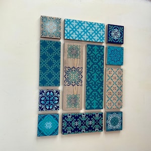 May include: A set of 12 teal and blue patterned wooden tiles with geometric designs. The tiles are arranged in a grid pattern on a white wall.
