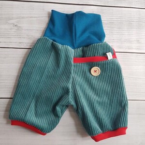 Puede incluir: Pantalones cortos de beb&eacute; de pana color turquesa con cintura alta turquesa y ribete rojo. Un bot&oacute;n de madera y un peque&ntilde;o bolsillo rojo detallan los pantalones cortos. Los pantalones cortos est&aacute;n etiquetados como "Luna & Lotte".