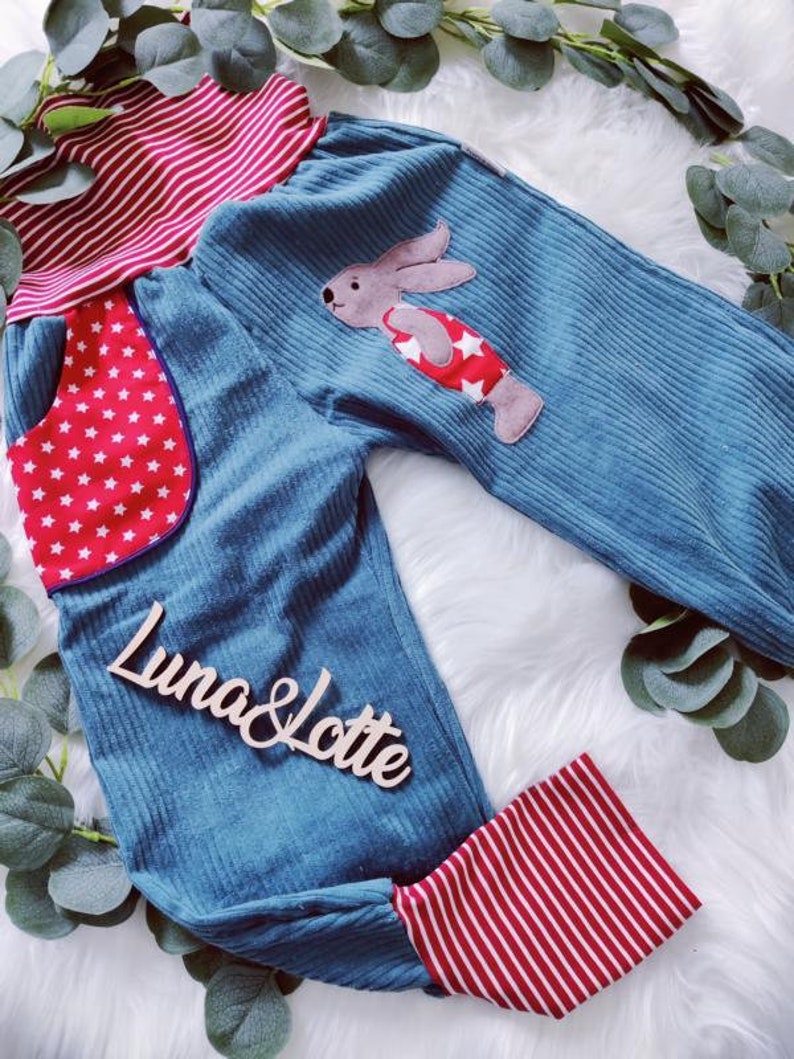May include: Blue corduroy pants with red and white striped cuffs and waistband. The pants have a red pocket with white stars and a felt bunny applique with red and white stars.