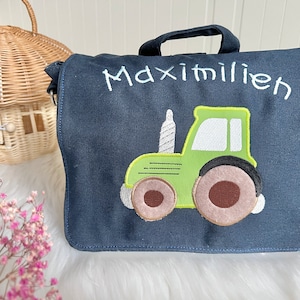Könnte beinhalten: Eine dunkelblaue Stofftasche mit einem grünen Traktor, der auf die Vorderseite gestickt ist. Die Tasche hat einen weißen gestickten Namen "Maximilien" über dem Traktor.