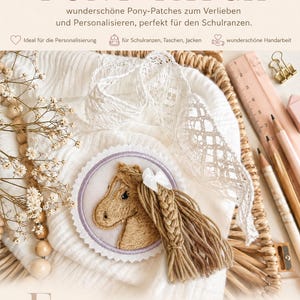Könnte beinhalten: Ein kreisförmiger, bestickter Aufnäher mit einem beigen Pferdekopf, einer geflochtenen Garnmähne und einer kleinen weißen Schleife. Der Aufnäher hat einen hellvioletten Rand und einen gezackten Saum auf weißem, strukturiertem Stoff mit Spitzenbesatz.