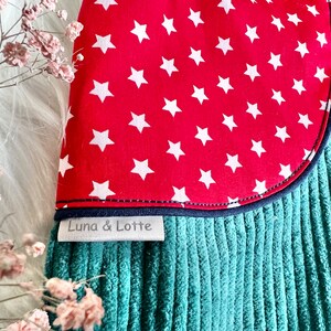 May include: A teal corduroy fabric with a red fabric patch sewn on. The patch has white stars on it. The fabric has a label that says "Luna & Lotte".