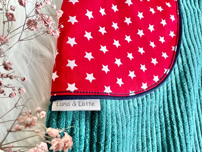 May include: A teal corduroy fabric with a red fabric patch sewn on. The patch has white stars on it. The fabric has a label that says "Luna & Lotte".