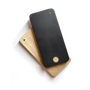 Könnte beinhalten: Zwei rechteckige Holzstücke, eines schwarz und eines hellbraun, liegen übereinander. Das schwarze Stück hat ein kleines Loch in der oberen linken Ecke und ein größeres Loch in der unteren rechten Ecke.