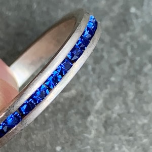 May include: A silver ring with a band of blue gemstones.