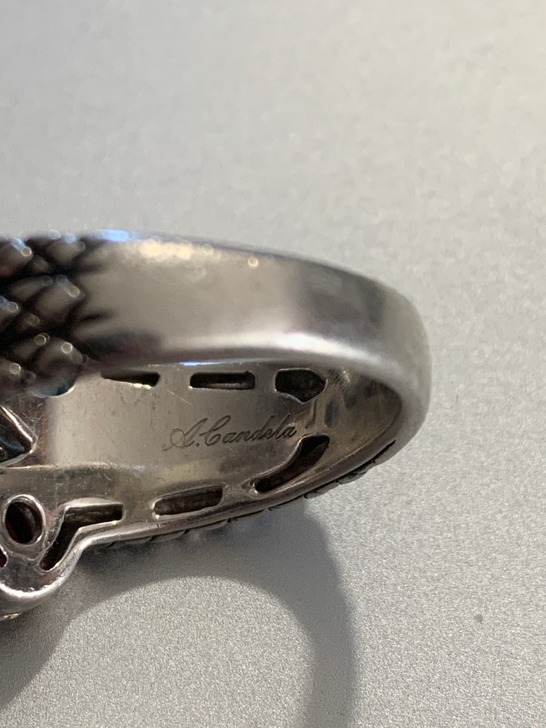 May include: Close-up of the inside of a silver ring with the inscription "A. Candela" on the band.
