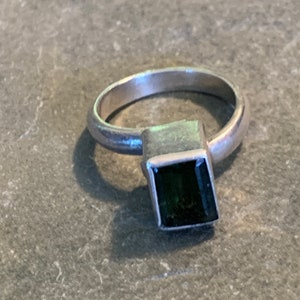 May include: A silver ring with a dark green square-shaped gemstone.