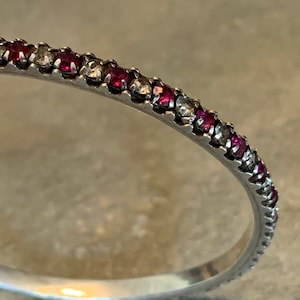 May include: A silver band ring with a row of small red and clear gemstones.