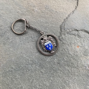 May include: Silver keychain with a circular charm featuring a coat of arms with the text "Wiesbaden" and blue and white enamel details.