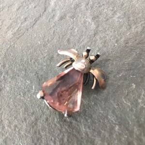 May include: A silver and gold tone bee brooch with a pink faceted glass stone.