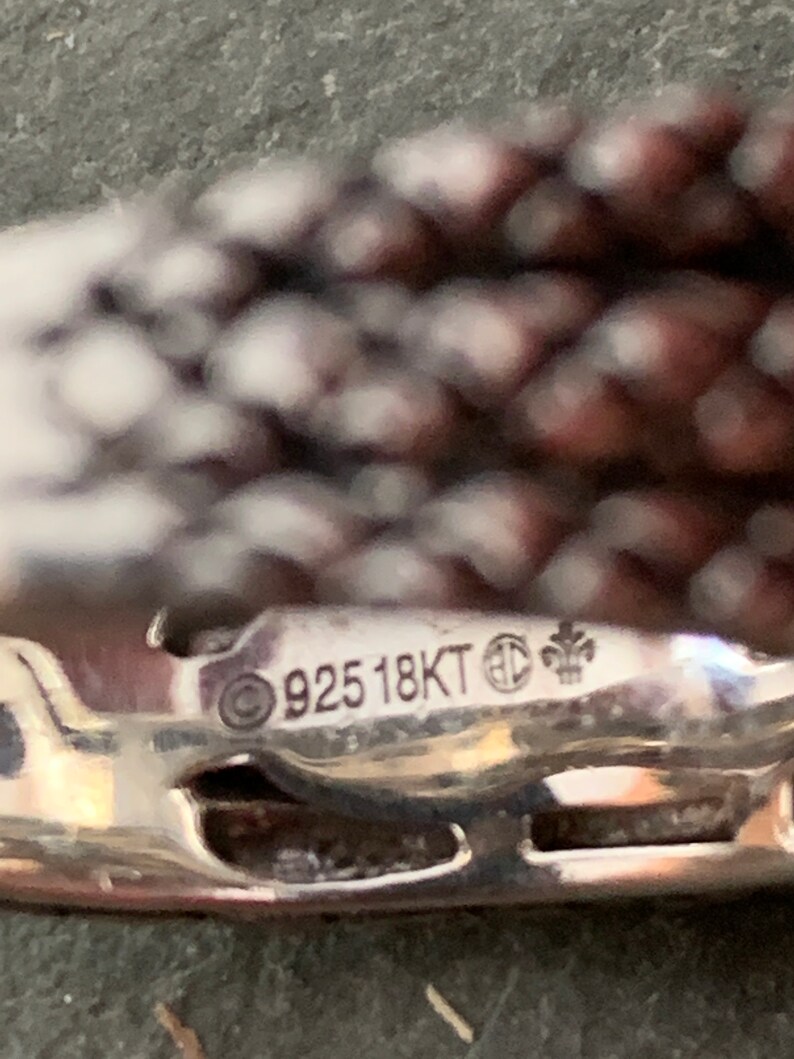 May include: Close-up of a silver metal tag with the inscription "925 18KT" and a symbol.