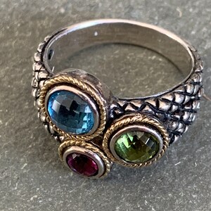 May include: A silver ring with a textured band and three gemstones. The gemstones are blue, green, and red.