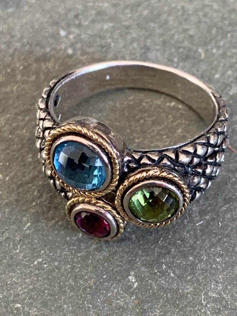May include: A silver ring with a textured band and three gemstones. The gemstones are blue, green, and red.