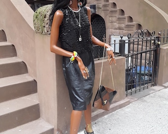 Puede incluir: Un top negro de lentejuelas con una falda de cuero negro y un bolso de mano negro y marrón. El maniquí lleva joyas doradas y zapatos de tacón de malla negra.