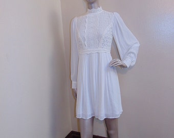 Puede incluir: Un vestido blanco con cuello alto y mangas largas. El vestido tiene un corpiño de encaje y una falda fluida.