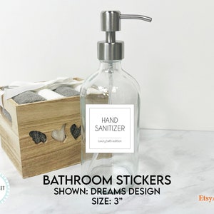 May include: A clear glass bottle with a silver pump dispenser and a white label that reads "HAND SANITIZER luxury bath edition". The bottle is sitting on a white surface. The label is 3 inches in size.  Bathroom stickers.