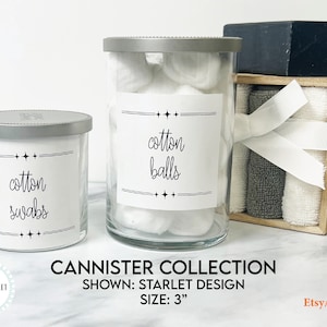 May include: Two glass canisters with silver lids and white labels. The labels have black text that reads "cotton balls" and "cotton swabs". The canisters are 3 inches tall and are part of a canister collection.