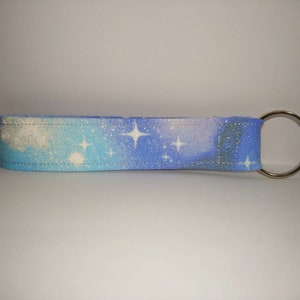 May include: A blue and white galaxy-themed fabric key chain with a silver key ring.