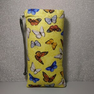 May include: A yellow drawstring bag with a butterfly print. The bag is made of fabric and has a drawstring closure. The butterflies are in various colors, including blue, orange, and yellow.