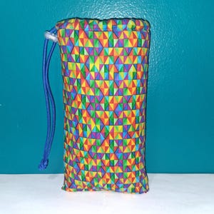 May include: A cylindrical drawstring pouch with a vibrant geometric pattern in red, orange, yellow, green, blue, and purple. The pouch has a blue drawstring closure and is likely used for storing small items.