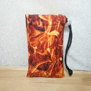 May include: A small drawstring bag with a black cord and a white button. The bag is made of a fabric with a fiery orange and yellow pattern.