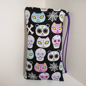 May include: Black drawstring bag with a colorful Day of the Dead themed print featuring sugar skulls, cats, and pandas. The bag has a purple drawstring.