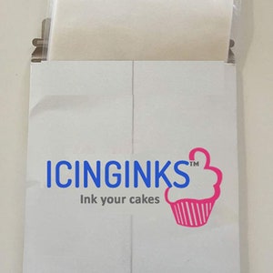 May include: A white cardboard package with the text "ICINGINKS" in blue and "Ink your cakes" below. A pink cupcake logo is on the right. A clear plastic bag is visible inside the package.