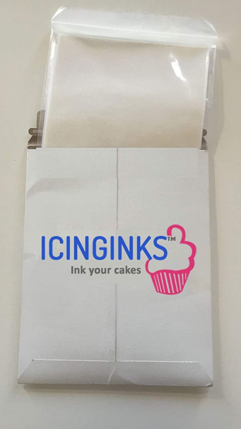 May include: A white cardboard package with the text "ICINGINKS" in blue and "Ink your cakes" below. A pink cupcake logo is on the right. A clear plastic bag is visible inside the package.