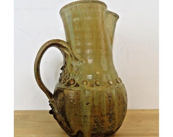 Jarra de cerámica hecha a mano, color verde oliva, con asa y detalles de arcilla esmaltada.