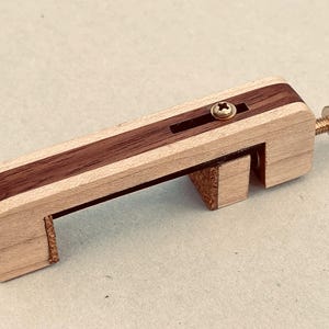 Könnte beinhalten: Eine Holzklammer mit einem dunkelbraunen Mittelstreifen und Messingbeschlägen. Die Klammer hat eine Schraube zur Breitenverstellung. Das Holz ist hell mit einem dunkelbraunen Akzent.