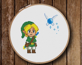 May include: A cross-stitch pattern featuring a green-clad character with blonde hair and a blue fairy with wings and a blue orb. The character is holding a sword and the fairy is leaving a trail of blue sparkles.