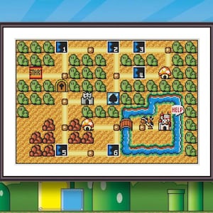 May include: A framed cross-stitch embroidery depicting a pixelated video game world map. The design features a yellow path, green bushes, red rocks, a blue river, a castle, and numbered blue squares. The text START and HELP are clearly visible.
