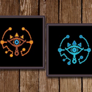 May include: Two framed images of the Sheikah Eye symbol from The Legend of Zelda: Breath of the Wild. The symbol is a stylized eye with a circle around it. The left image has an orange and yellow symbol on a black background. The right image has a blue symbol on a black background.