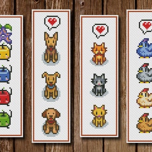 Könnte beinhalten: Vier handgefertigte Kreuzstich-Lesezeichen mit pixeligen Designs. Die Lesezeichen zeigen verschiedene Themen, darunter Früchte, Hunde, Katzen und Hühner. Jedes Lesezeichen hat einen weißen Rand und ist vor einem Holzgrund platziert.