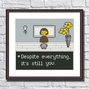 May include: A pixel art cross-stitch pattern featuring a character from the video game Undertale. The character is standing in front of a mirror with a yellow flower in a vase to the right. The text below reads "*Despite everything, it's still you."