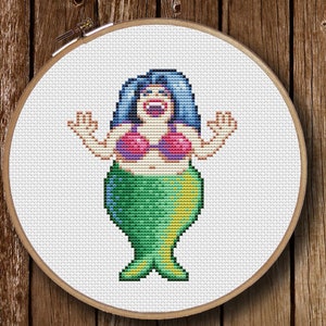 Puede incluir: Patrón de punto de cruz de una sirena con cabello azul, un sujetador rosa y una cola verde y amarilla. La sirena está sonriendo y tiene los brazos levantados en el aire.