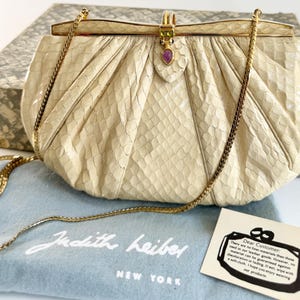 Bolso vintage Judith Leiber, estuche original, bolsa guardapolvo, color blanco roto, de piel de serpiente, convertible, cierre joya morado y verde, correa de cadena dorada.