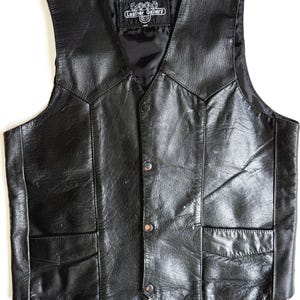 Op de afbeelding: Zwarte leren vest met een V-hals, twee voorzakken en drie knoopsluitingen. Het vest heeft een satijnen voering en een label met de tekst "Leather Gallery". Een klassieke stijl.
