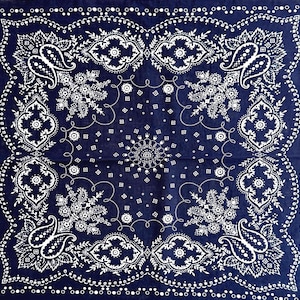 May include: A navy blue bandana with a white paisley and floral design. The square cloth features a detailed border with small white dots. The center has a symmetrical pattern with a central floral design and paisley elements.