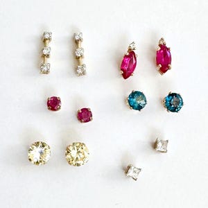 May include: Assortment of earrings with various gemstones, including ruby, sapphire, and diamond. The earrings are in gold settings and feature different shapes, including round, square, and marquise.