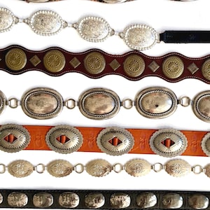 Op de afbeelding: Acht horizontaal gestapelde riemen. De riemen hebben diverse ontwerpen, waaronder zilverkleurige ovale concho's, messingkleurige ronde studs en gladde metalen platen op leren banden in tinten zwart, bruin en tan.