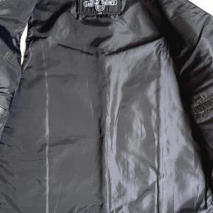 Op de afbeelding: Zwarte leren vest met een zwarte satijnen voering. De binnenkant heeft een label met de tekst "Leather Gallery". Het vest is open en toont de binnenvoering en stikdetails. Een klassiek bovenkledingstuk.