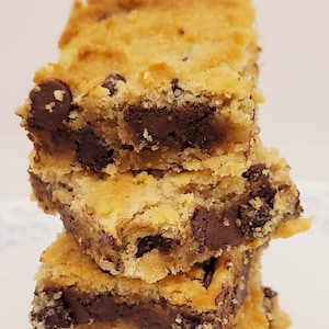 May include: A stack of three golden brown chocolate chip cookie bars with chocolate chips visible throughout the bars.