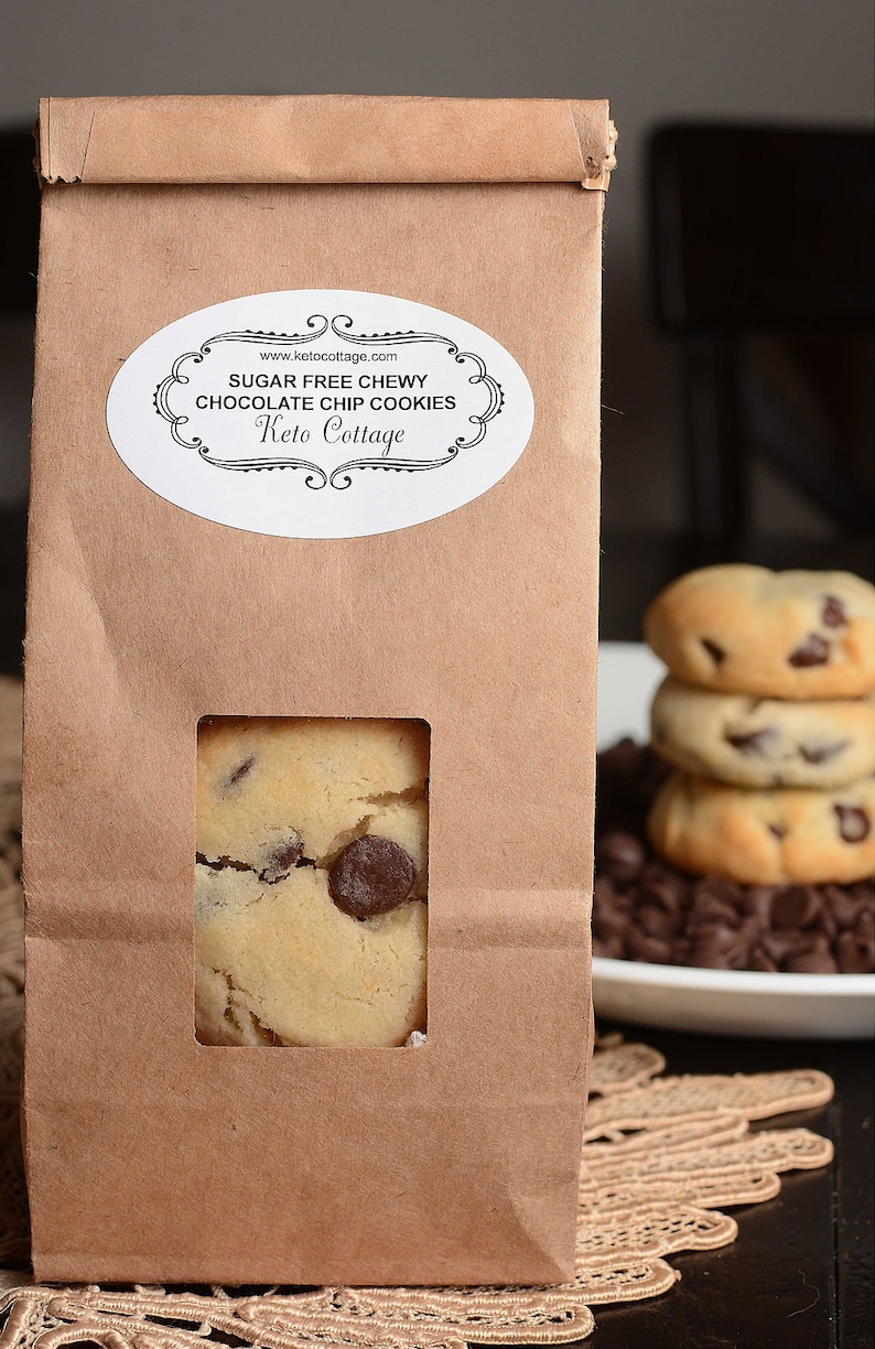 May include: A brown paper bag with a white label that reads "Sugar Free Chewy Chocolate Chip Cookies Keto Cottage" and a window showing a chocolate chip cookie.