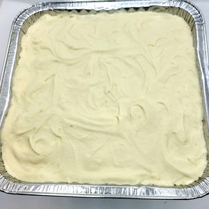 May include: A white, creamy substance is spread evenly in a silver, rectangular baking pan. The substance has a smooth, swirled texture.