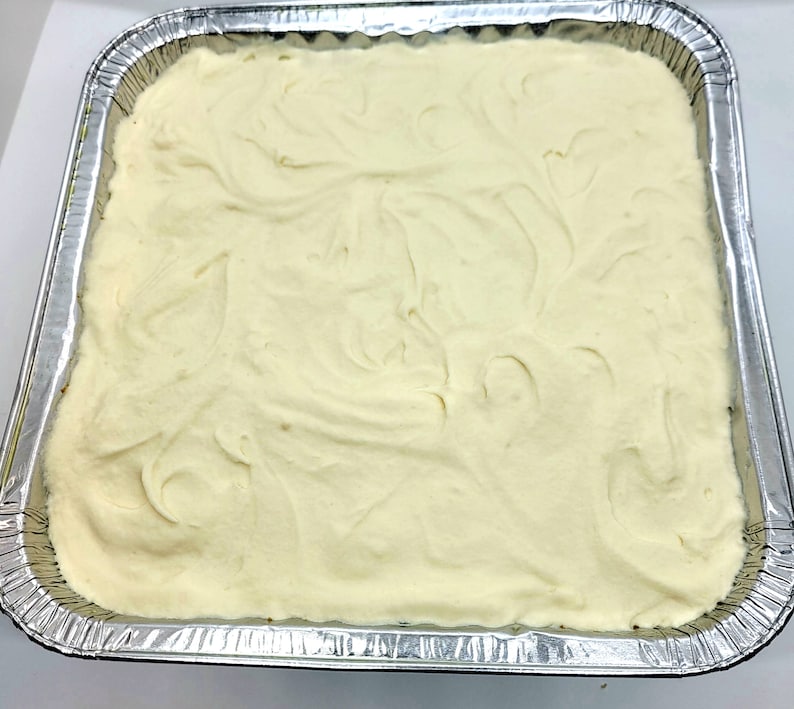 May include: A white, creamy substance is spread evenly in a silver, rectangular baking pan. The substance has a smooth, swirled texture.