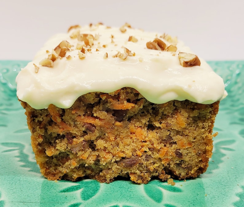 May include: A close-up of a frosted carrot cake with pecans on top. The cake is cut in half and the inside is visible, showing the orange carrot pieces.