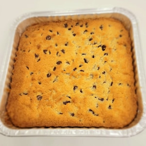May include: A golden brown cookie bar with chocolate chips in a silver baking pan.