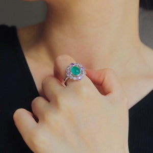 May include: A silver ring with a green gemstone surrounded by smaller pink and white gemstones.