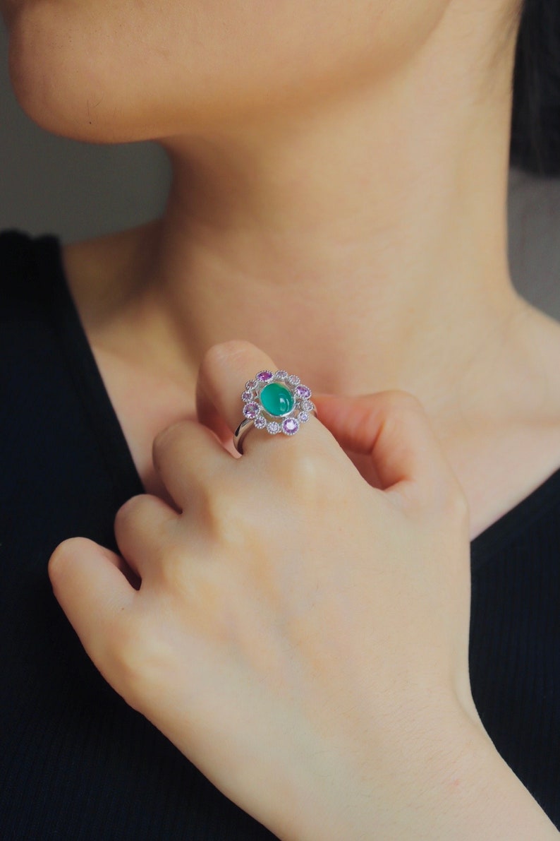May include: A silver ring with a green gemstone surrounded by smaller pink and white gemstones.